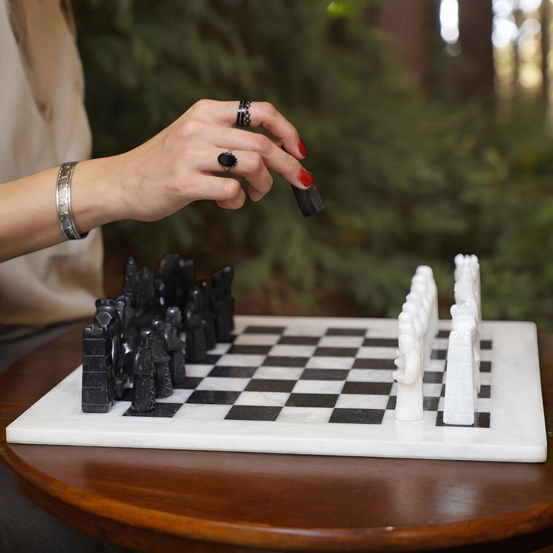 White and Black Marble Statue Chess Set Placing on the table and a women hand making move 