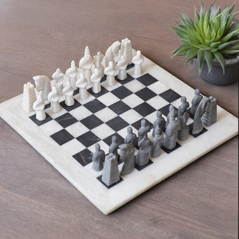white and black matt antique marble chess set placing on the floor and a little plant beside